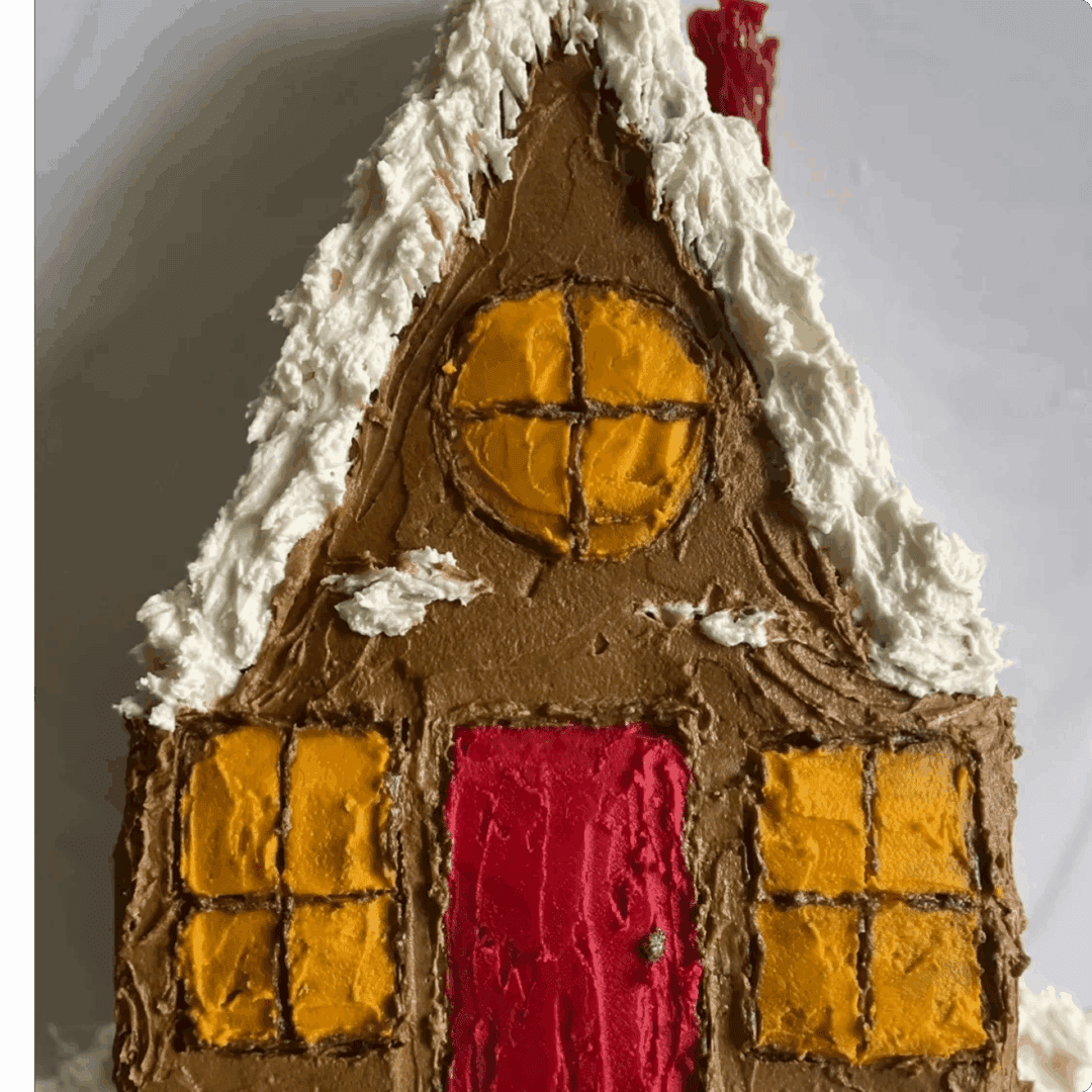 A gingerbread house with yellow windows and a red door, decorated with white icing.