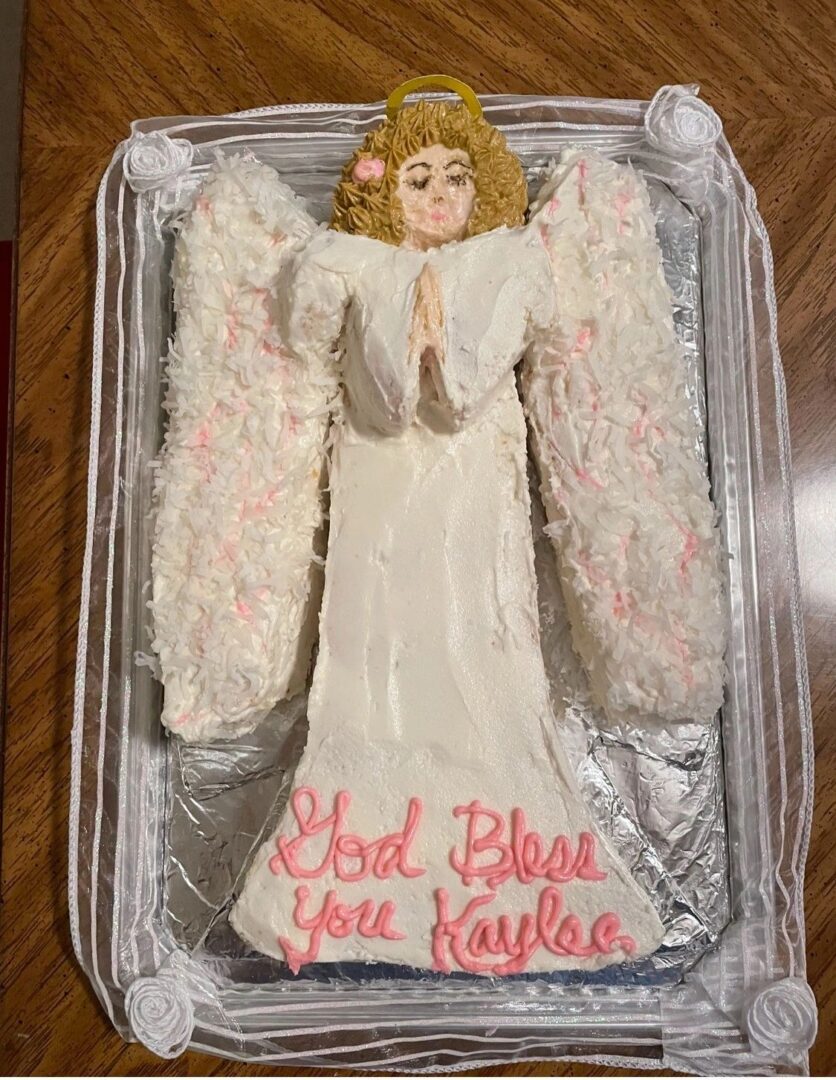 An angel-shaped cake with white icing and pink details.