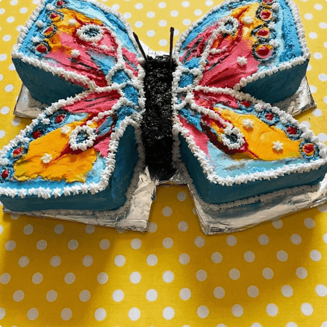 Colorful butterfly-shaped cake with intricate icing details on a yellow polka dot tablecloth.