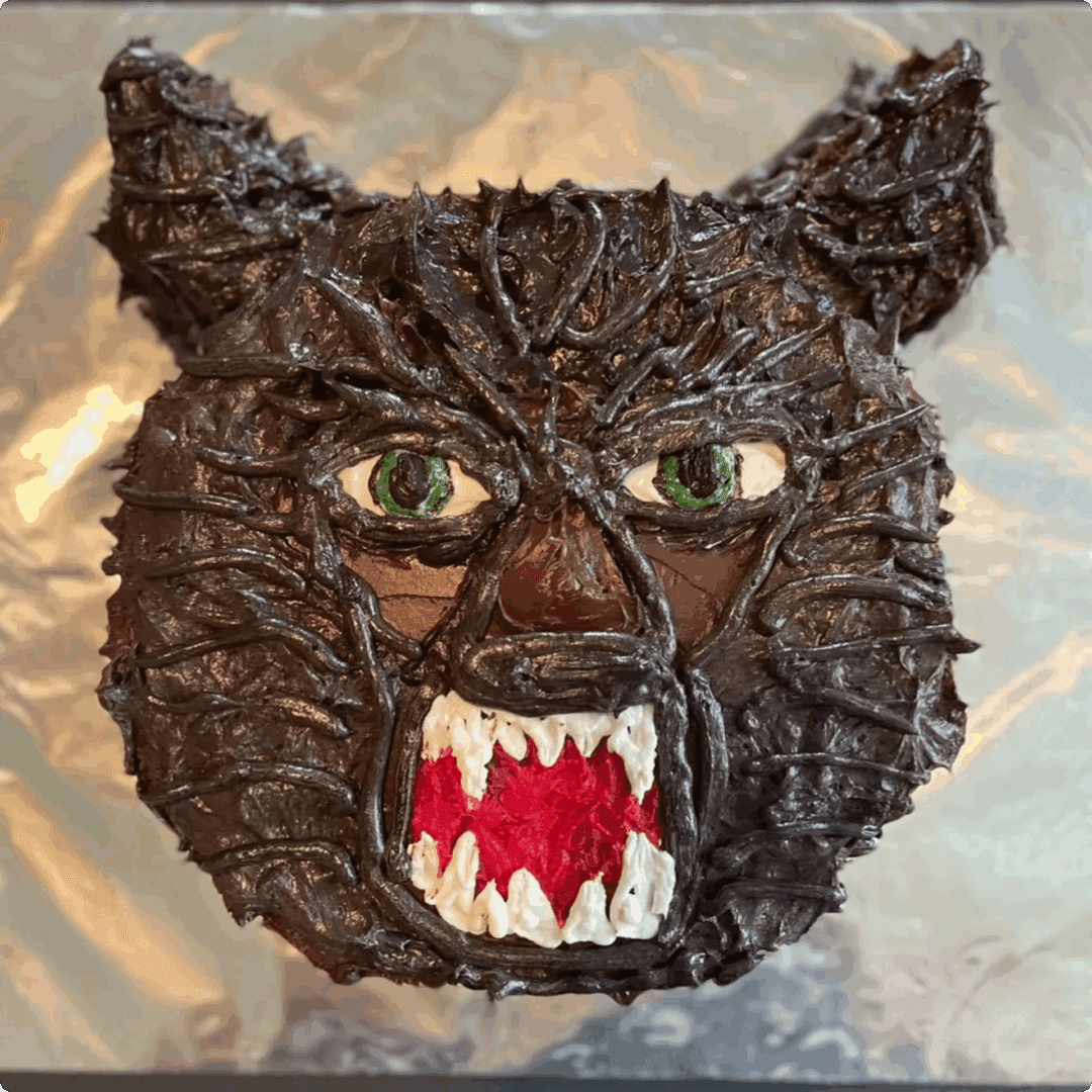 A fierce chocolate cat face with green eyes and sharp red teeth.
