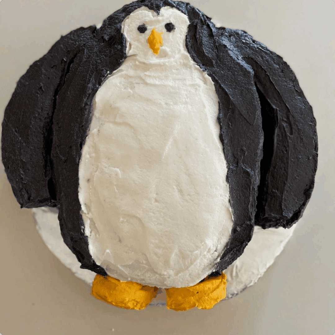 A penguin-shaped cake with black, white, and yellow frosting.