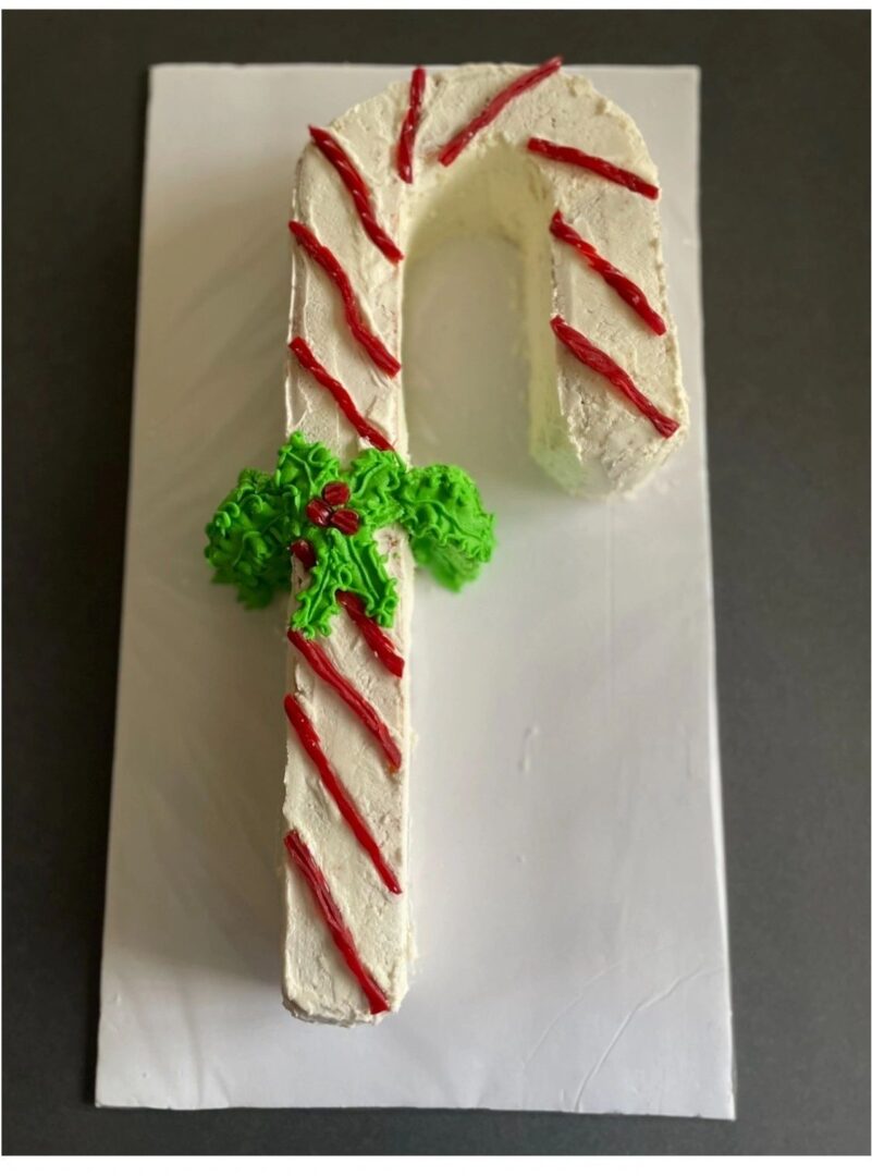 Candy cane-shaped cake decorated with red stripes and green leaves.