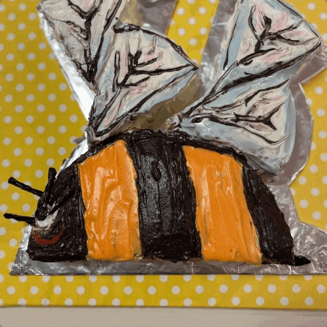 A cute handmade bee craft with black and orange stripes on a yellow polka-dot background.