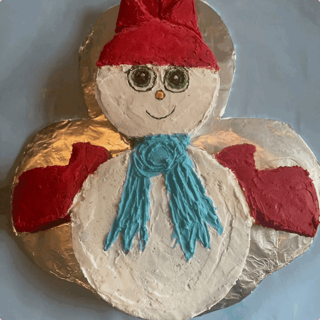 A snowman-shaped cake decorated with frosting and a red hat.