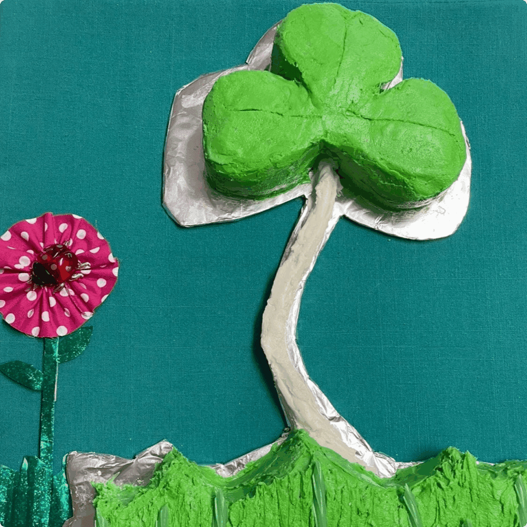 A handmade four-leaf clover and pink flower craft on green paper.