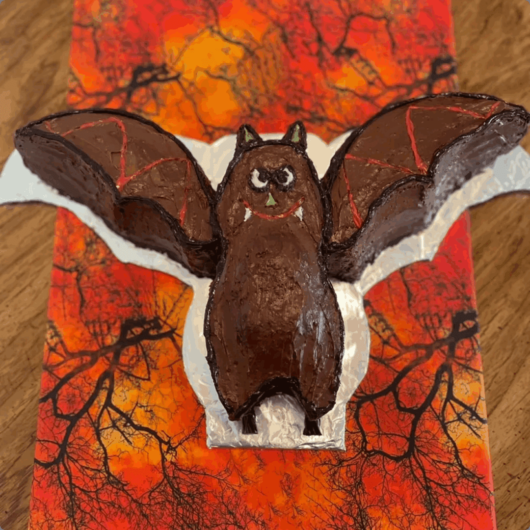 A bat-shaped cookie on a colorful autumn-themed plate.
