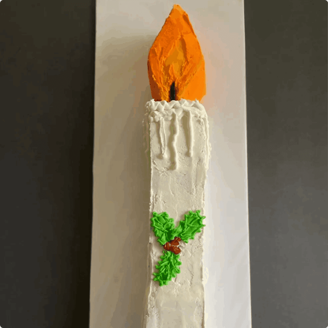 A tall white candle with an orange flame and green holly decoration.