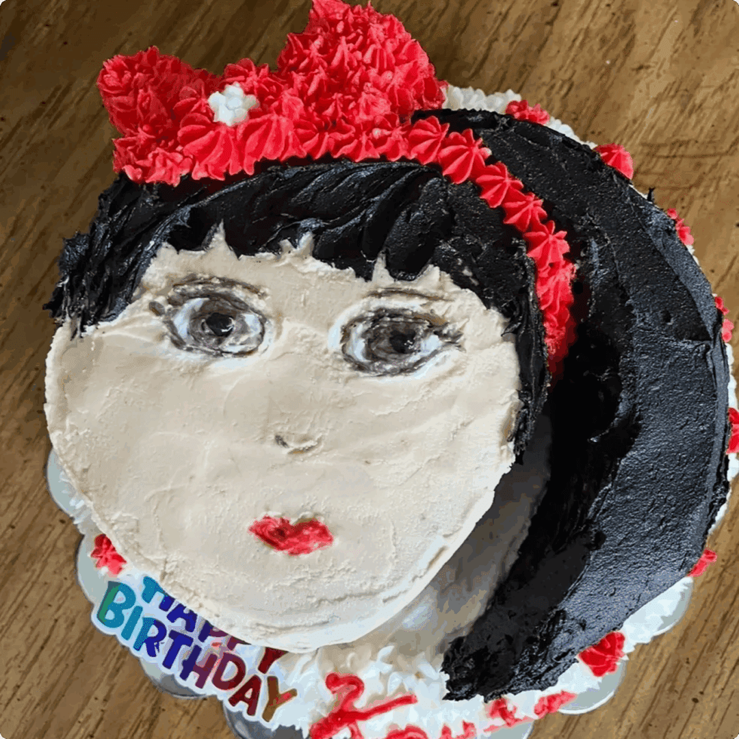 A cake decorated as a girl's face with a red bow and birthday text.